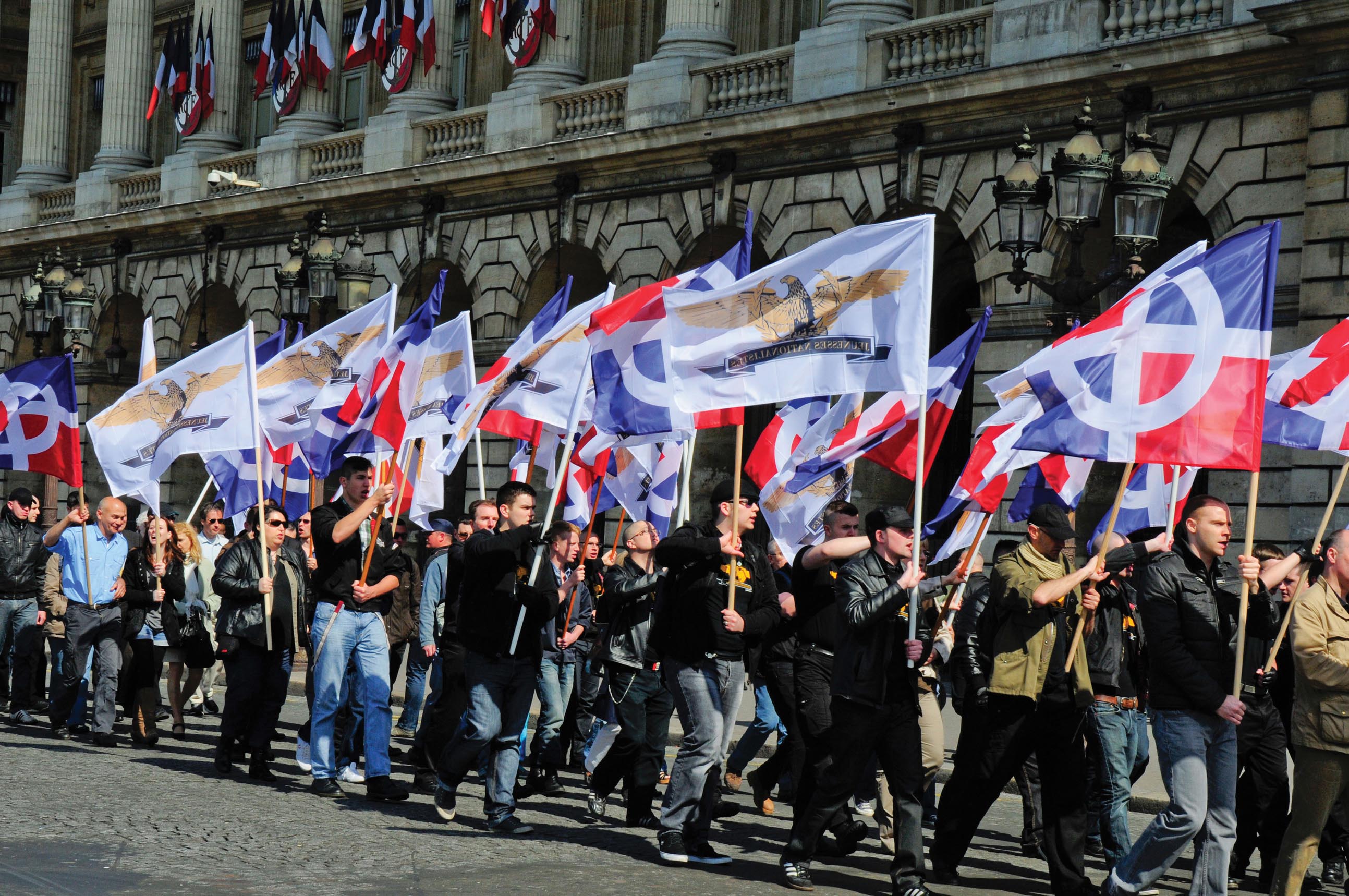 A group of people carrying flags and marching in Rue de Rivoli in Paris, France.