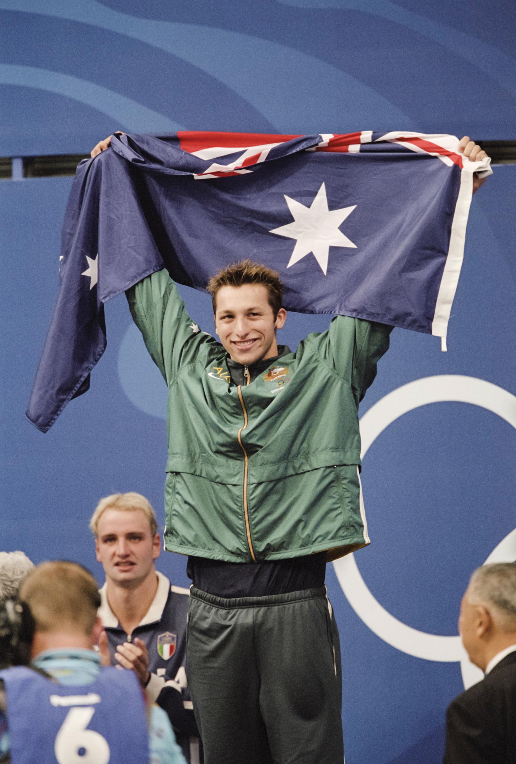 Olympic gold-medalist Ian Thorpe holding up the Australian flag above his head as he stands on the podium.