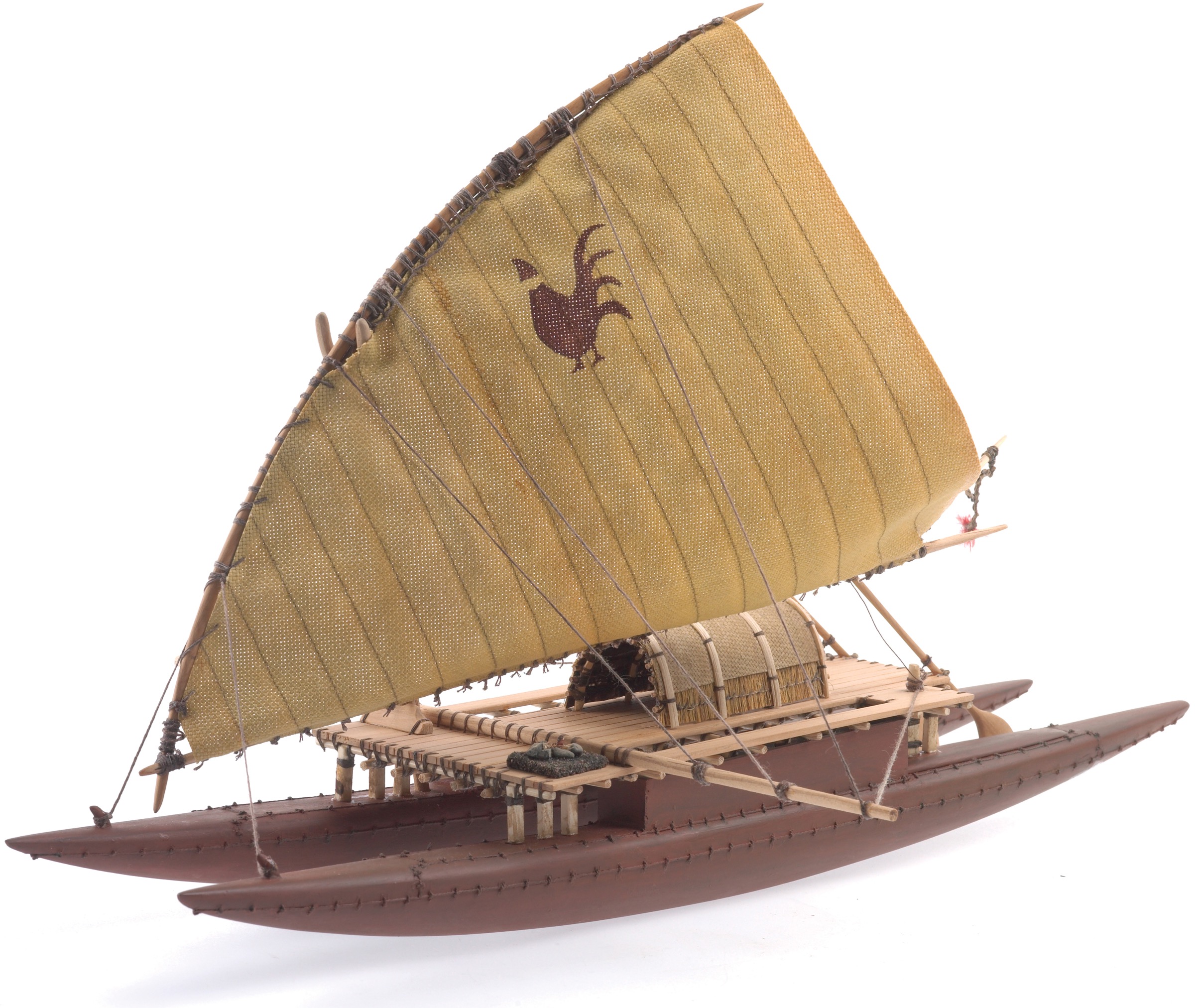 A wooden model shows a double-hulled sailing canoe, with a large sail, tapering forward and down.