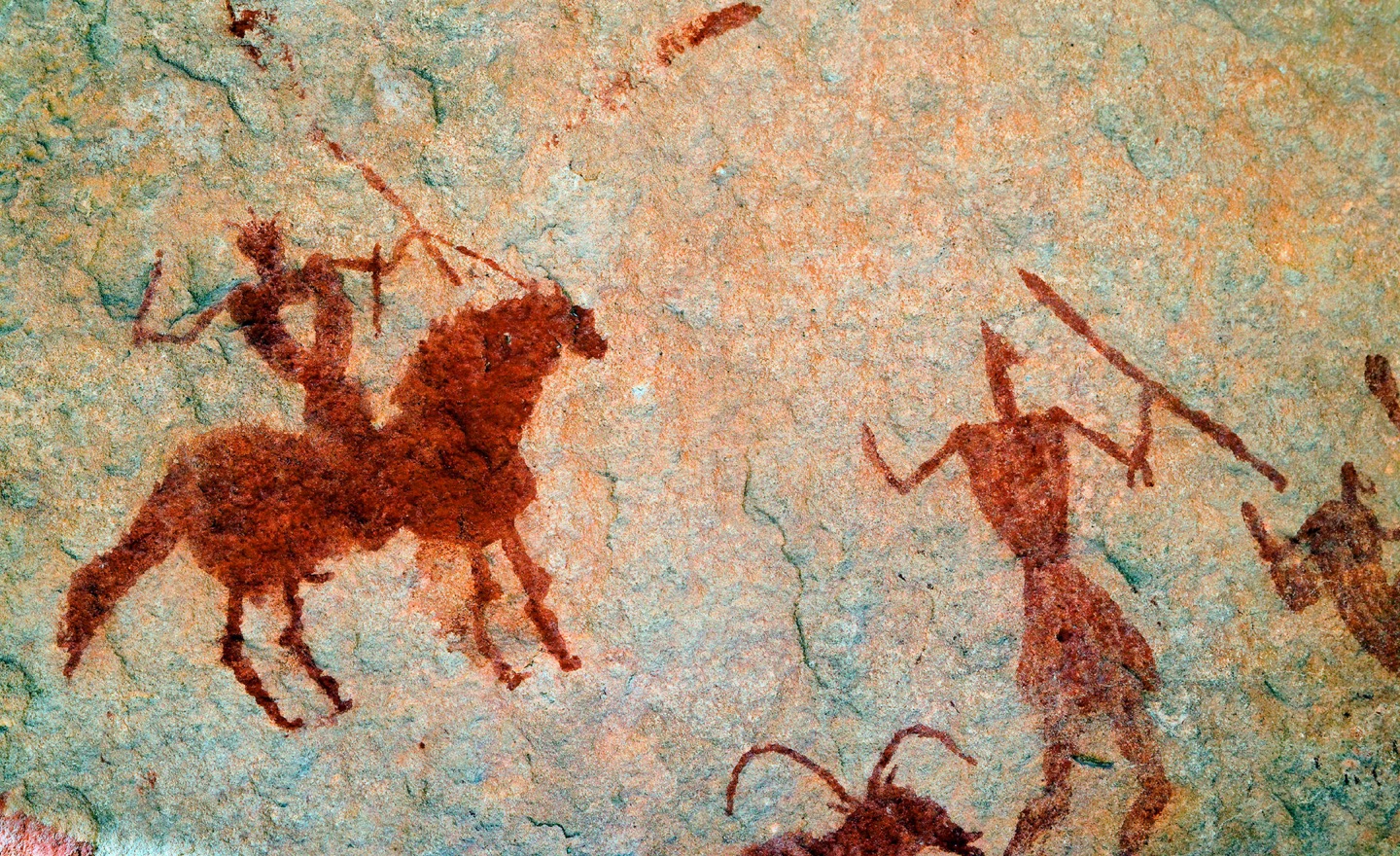 A cave painting depicts a man seated on a horse, holding a sword and facing a man on foot, holding a spear.