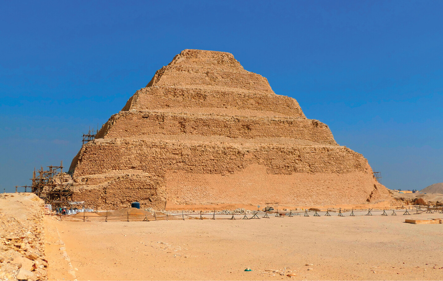 A pyramid with six rising tiers. Sand has piled up along the flat edges of the pyramid, obscuring the shape in the center.
