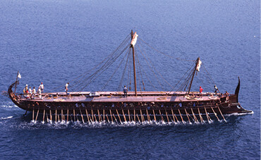 A modern replica of an Athenian trireme warship being rowed through the ocean.
