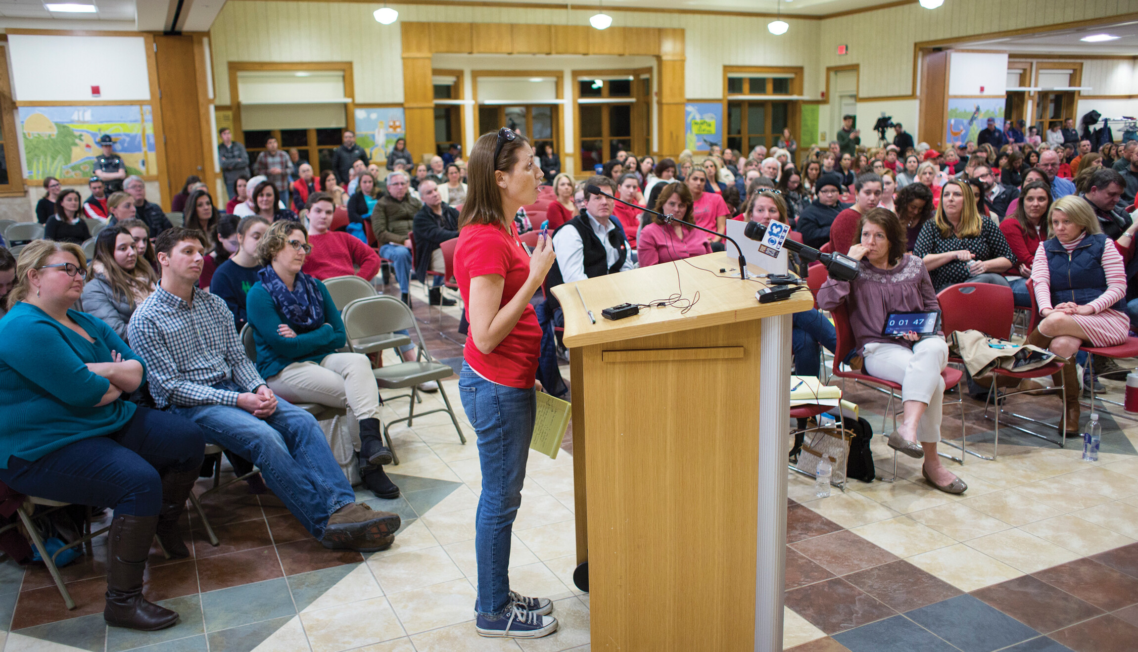 A woman stands and speaks into the mic of a podium in an auditorium.