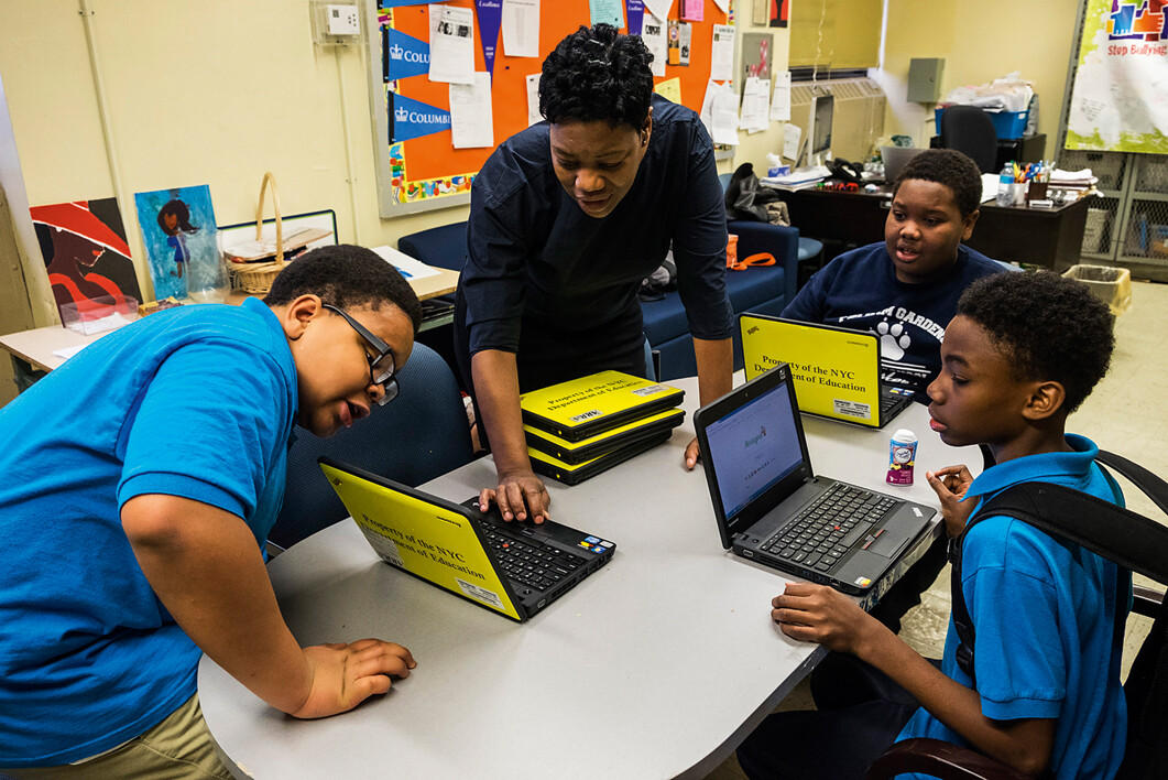 Three boys and their teacher working on laptops in a classroom.