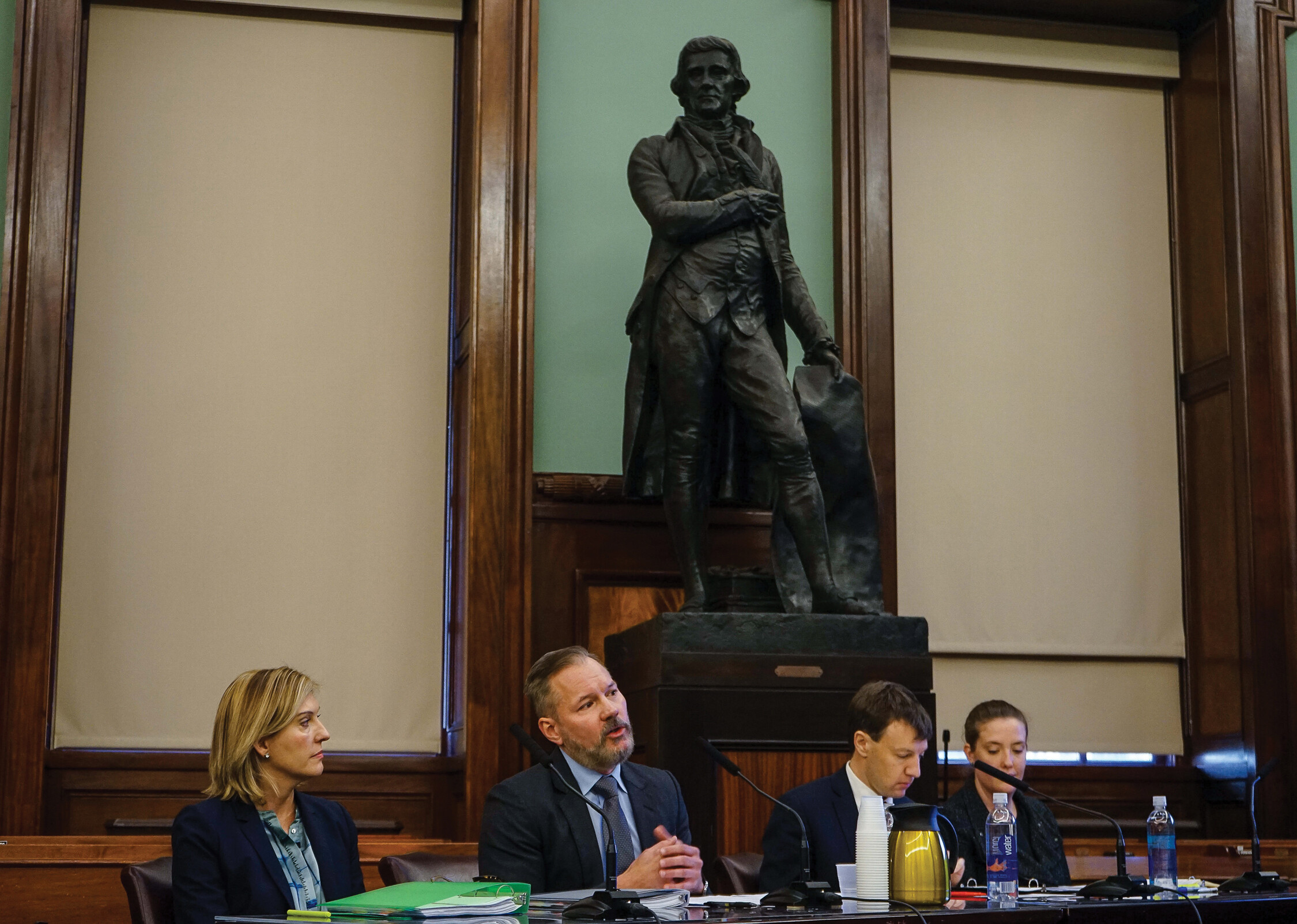 City council members sit in session as a statue of Thomas Jefferson looks on.