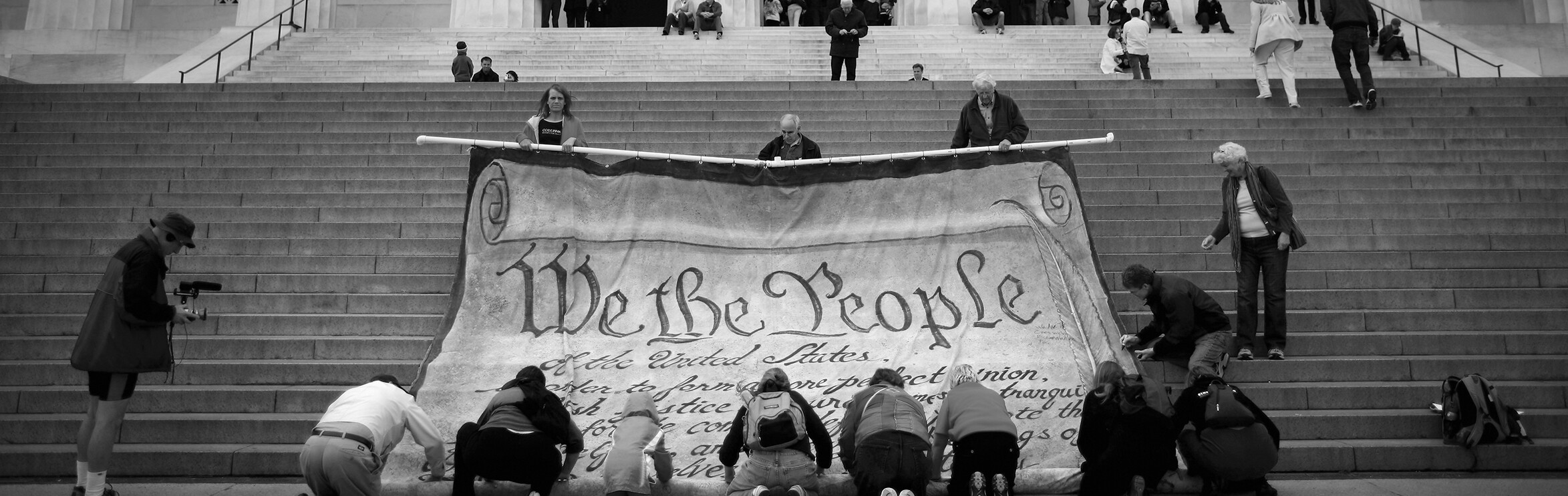 On the steps of Washington’s Lincoln Memorial, a team of people furls a giant copy of the preamble to the U S Constitution.