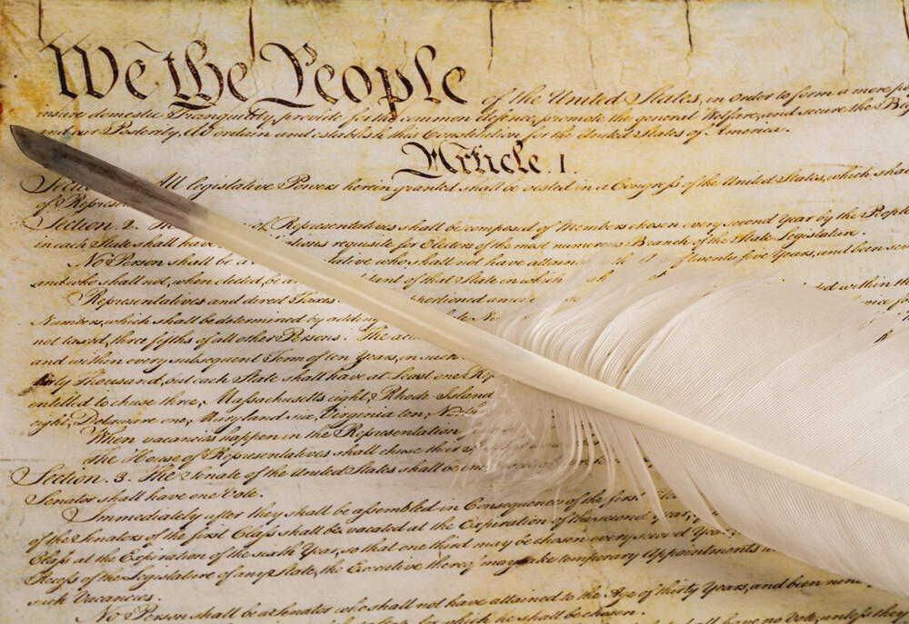 A quill pen rests atop a copy of the Constitution.