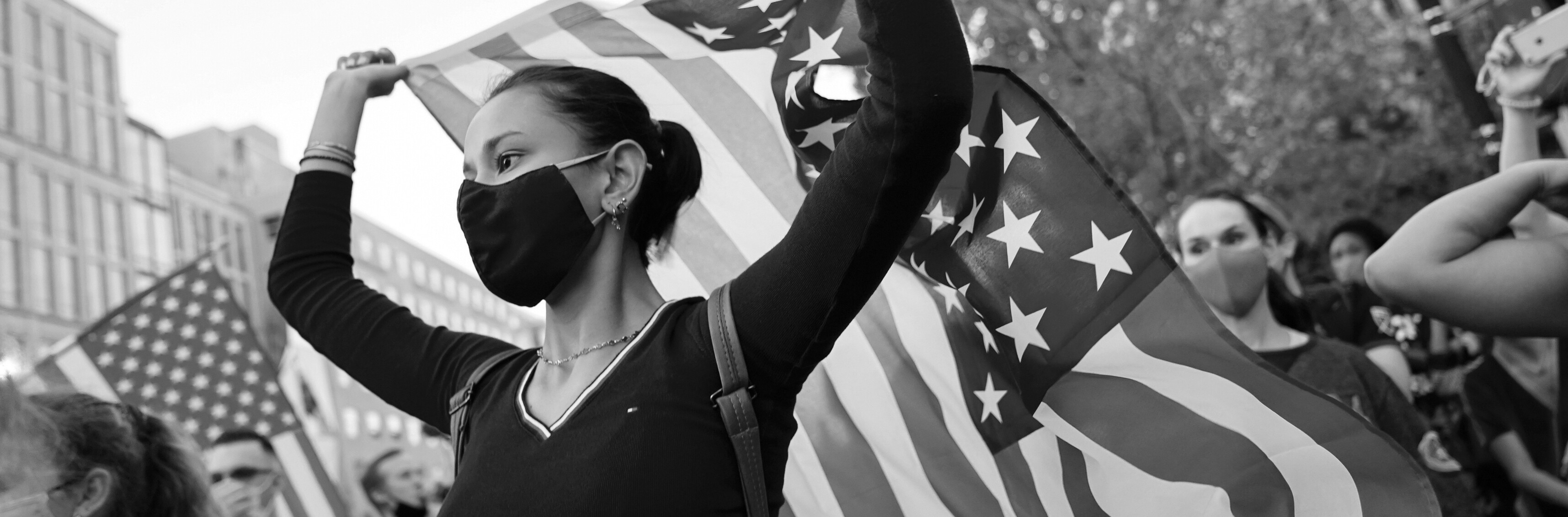 A young woman and several others wave flags at an outdoor gathering.