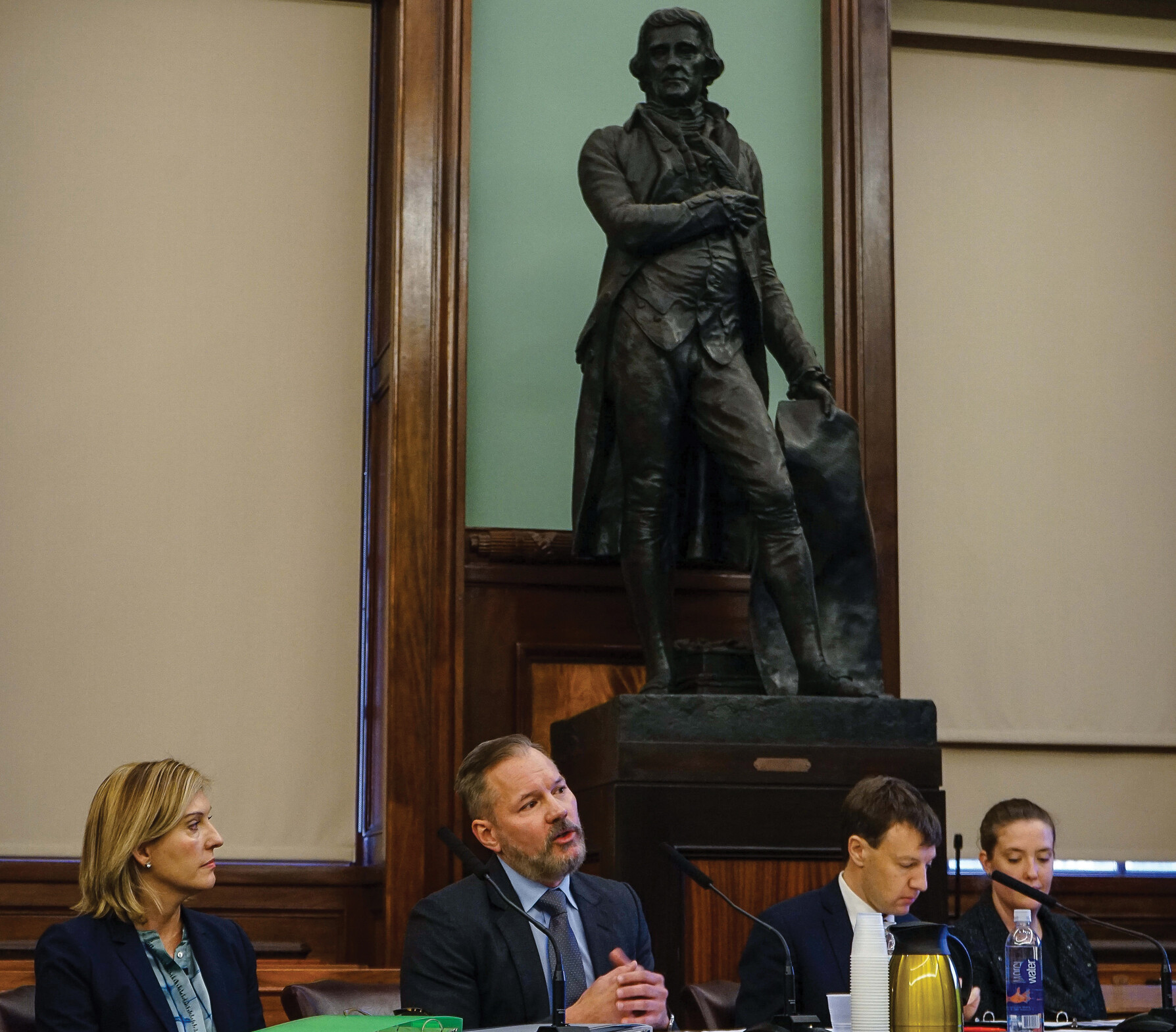 City council members sit in session as a statue of Thomas Jefferson looks on.
