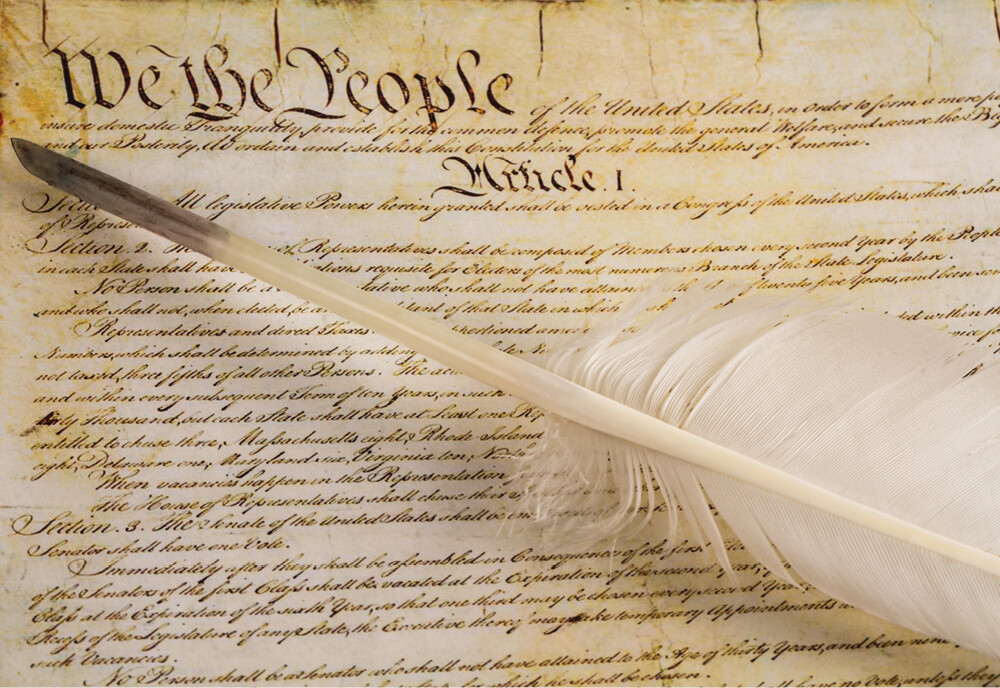 A quill pen rests atop a copy of the Constitution.