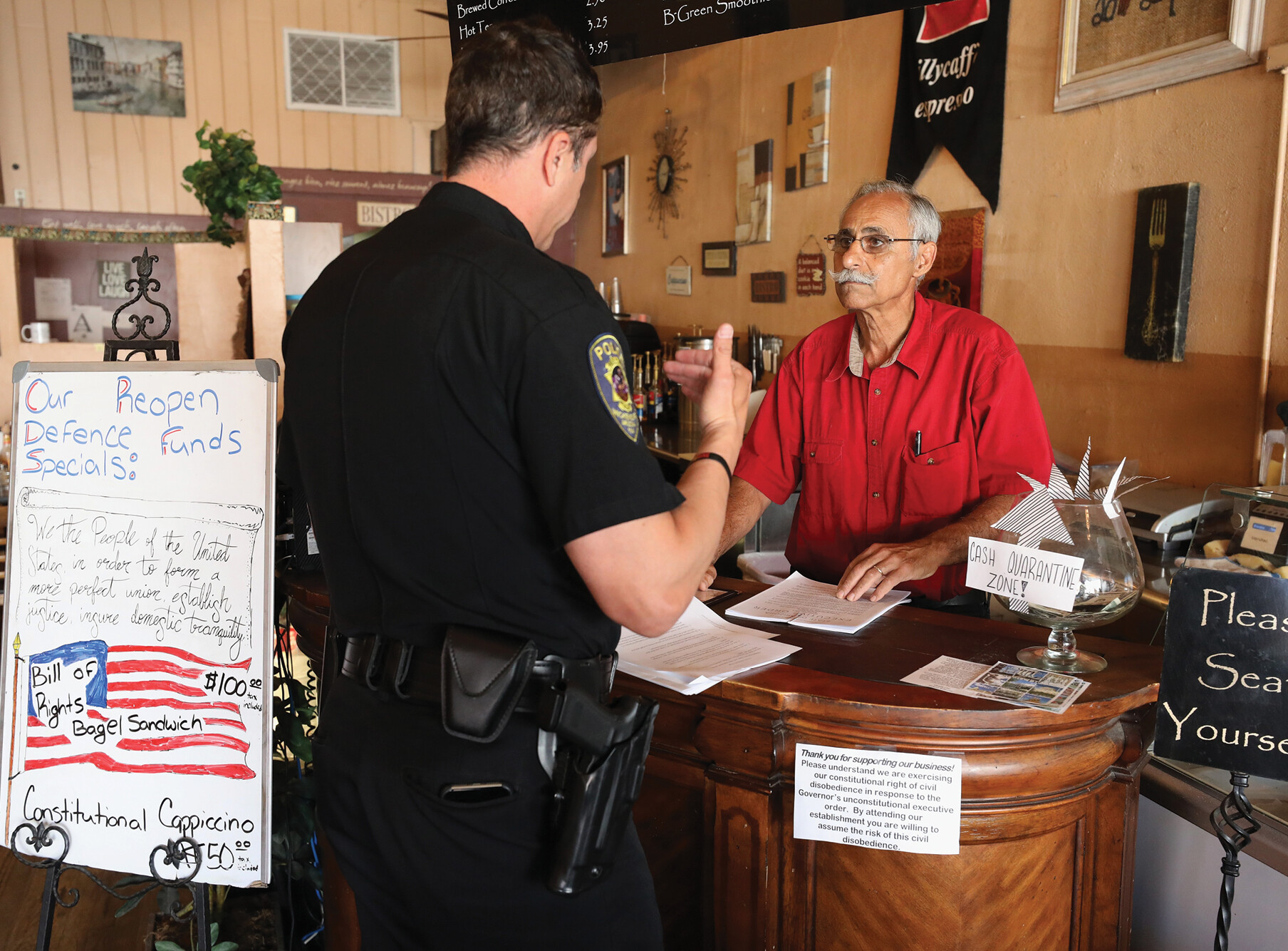 A photo shows a man behind a bakery counter speaking to a police officer.