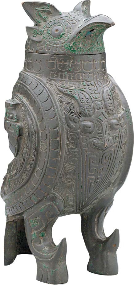 A bronze ceremonial drinking vessel shaped like a bird with elaborate carvings up and down its body.