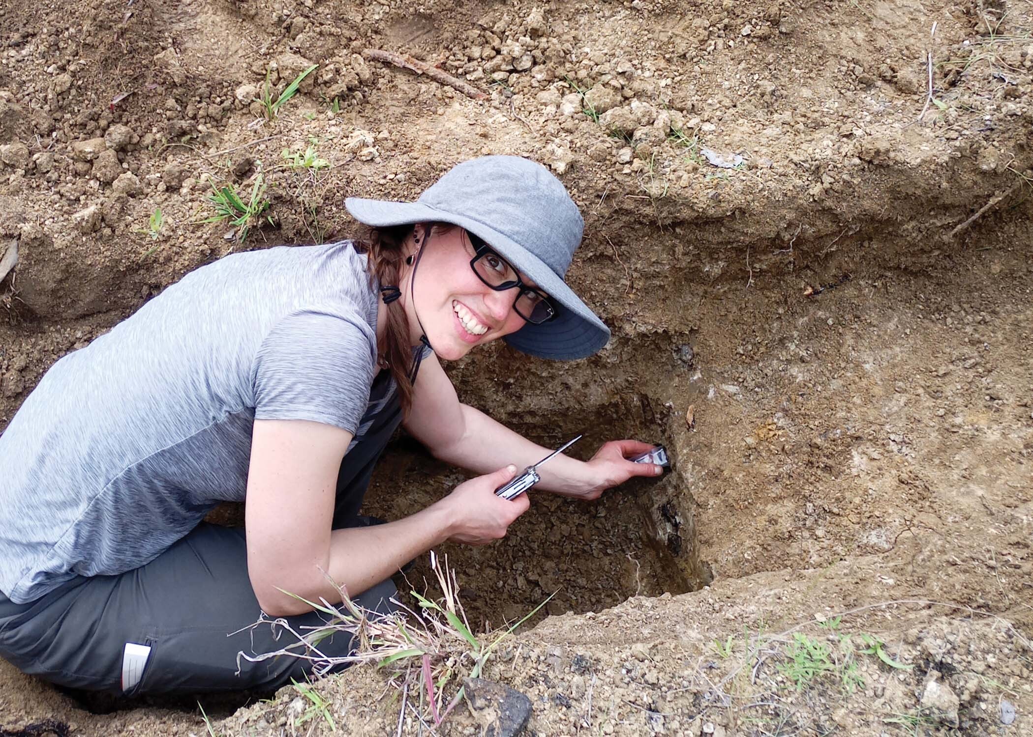 A researcher sits on the ground at an archeological site.