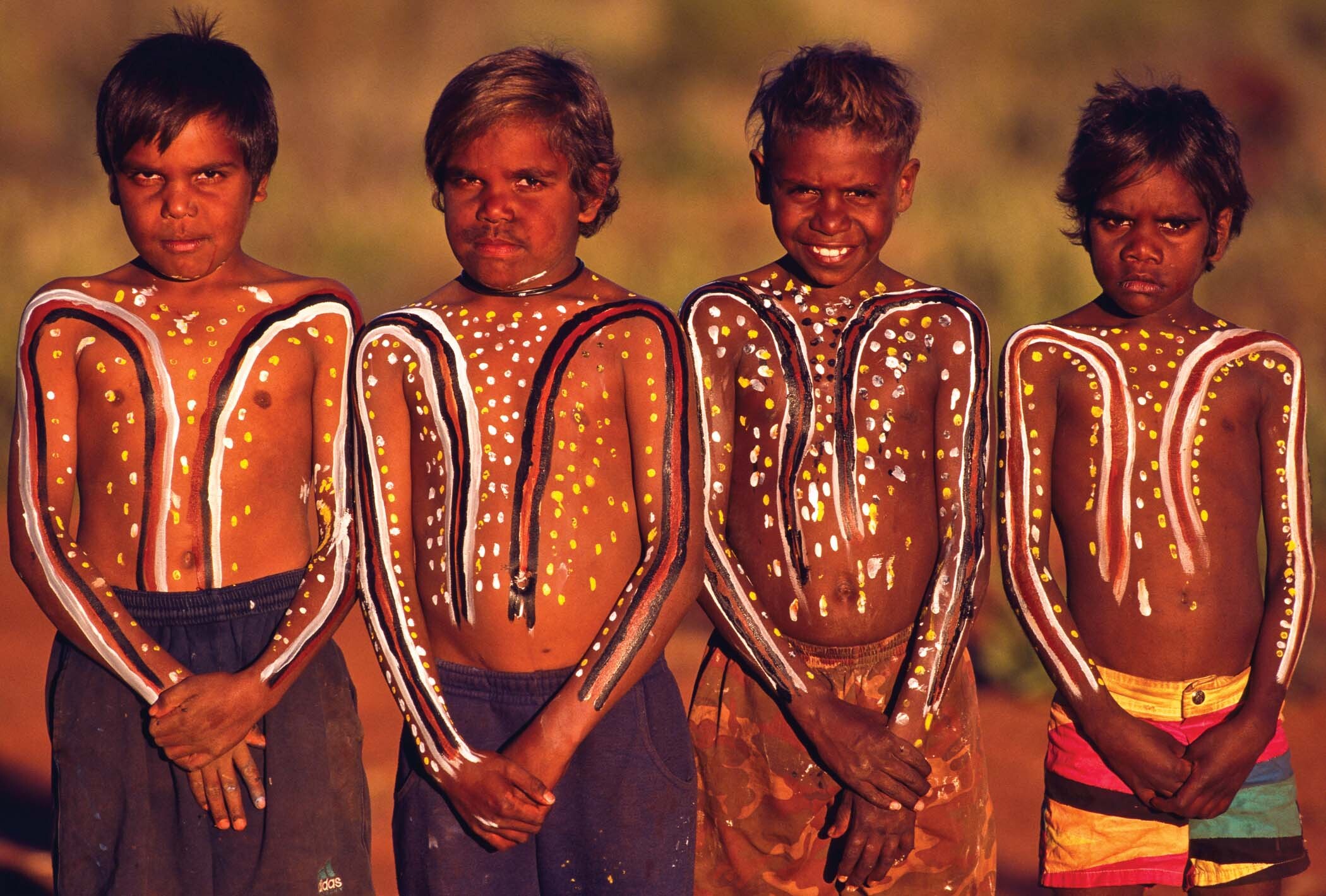 Four aboriginal boys with their torsos and arms painted with animistic designs.