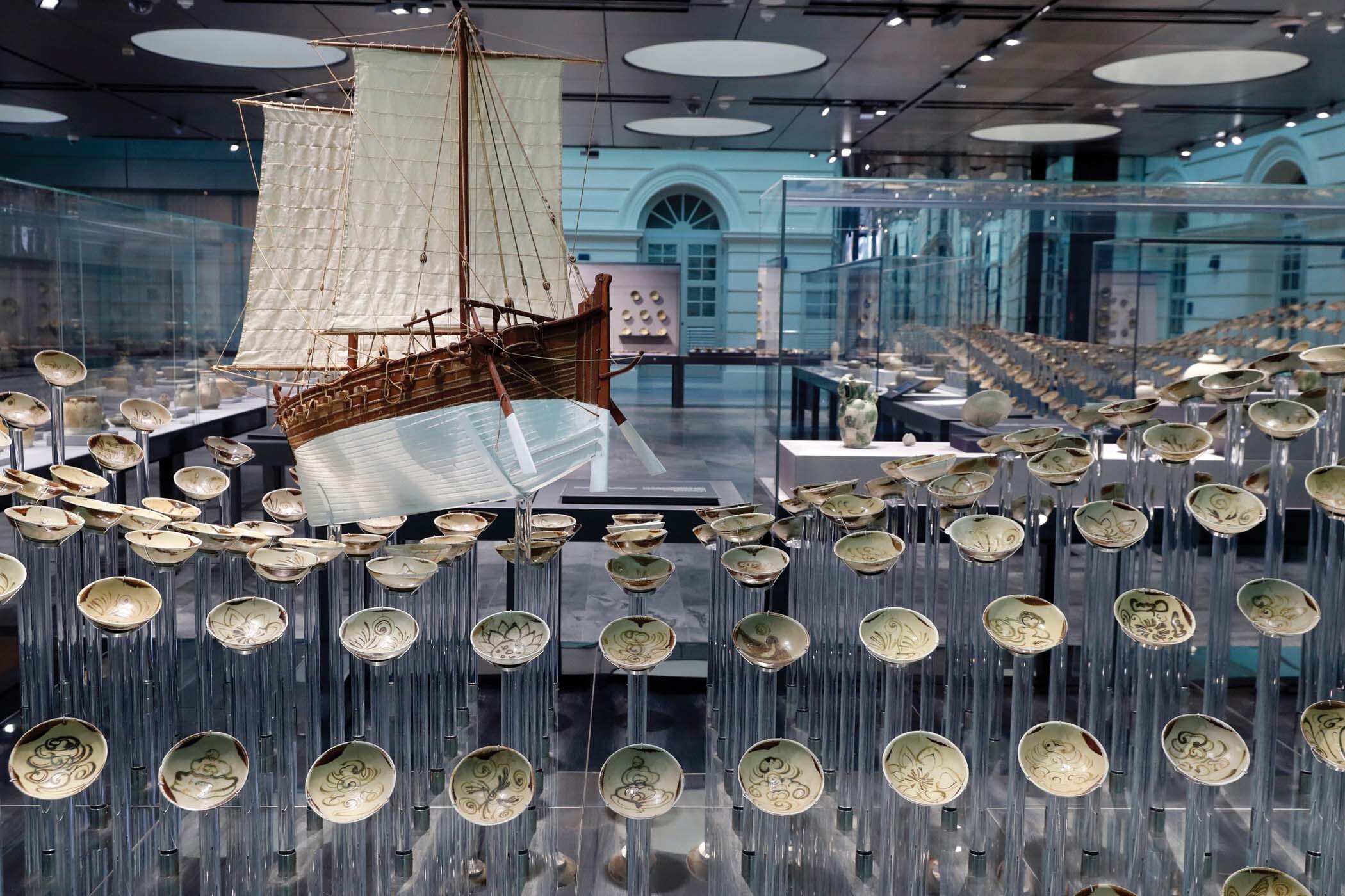 A photo of an exhibition of a wave of ceramics bowls on risers with a model ship in the center.