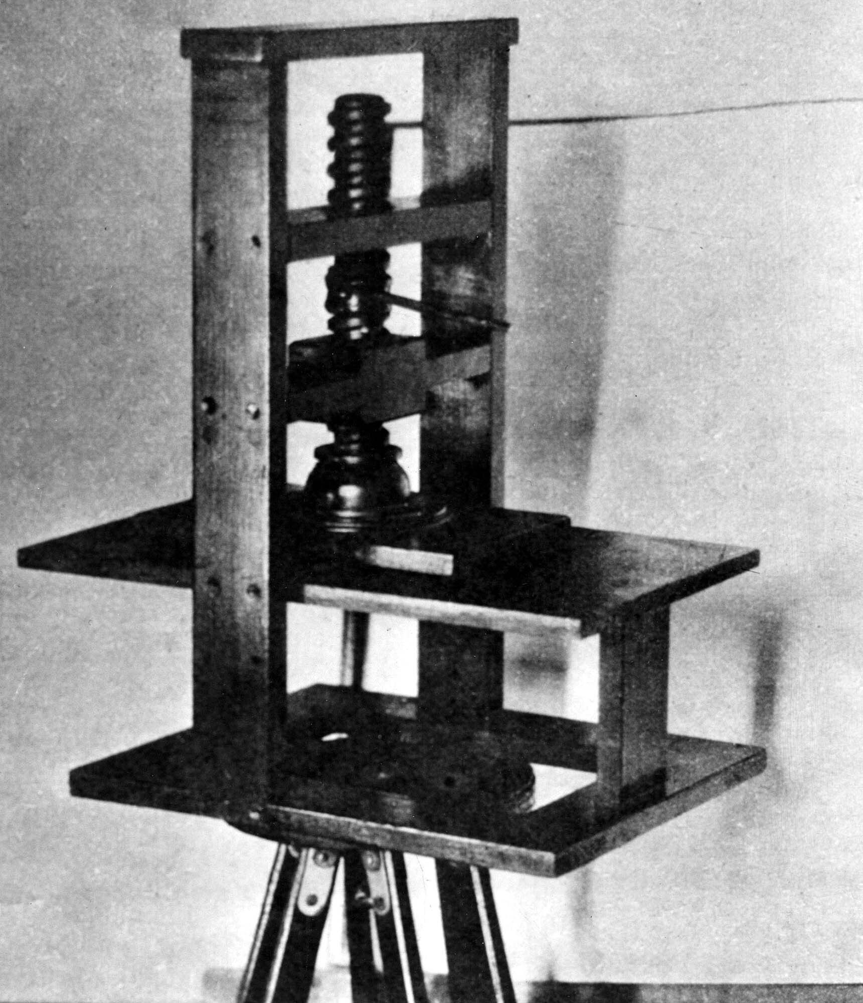 A black-and-white photo shows a Gutenberg printing press. The press has a large vertical screw to push two plates together.
