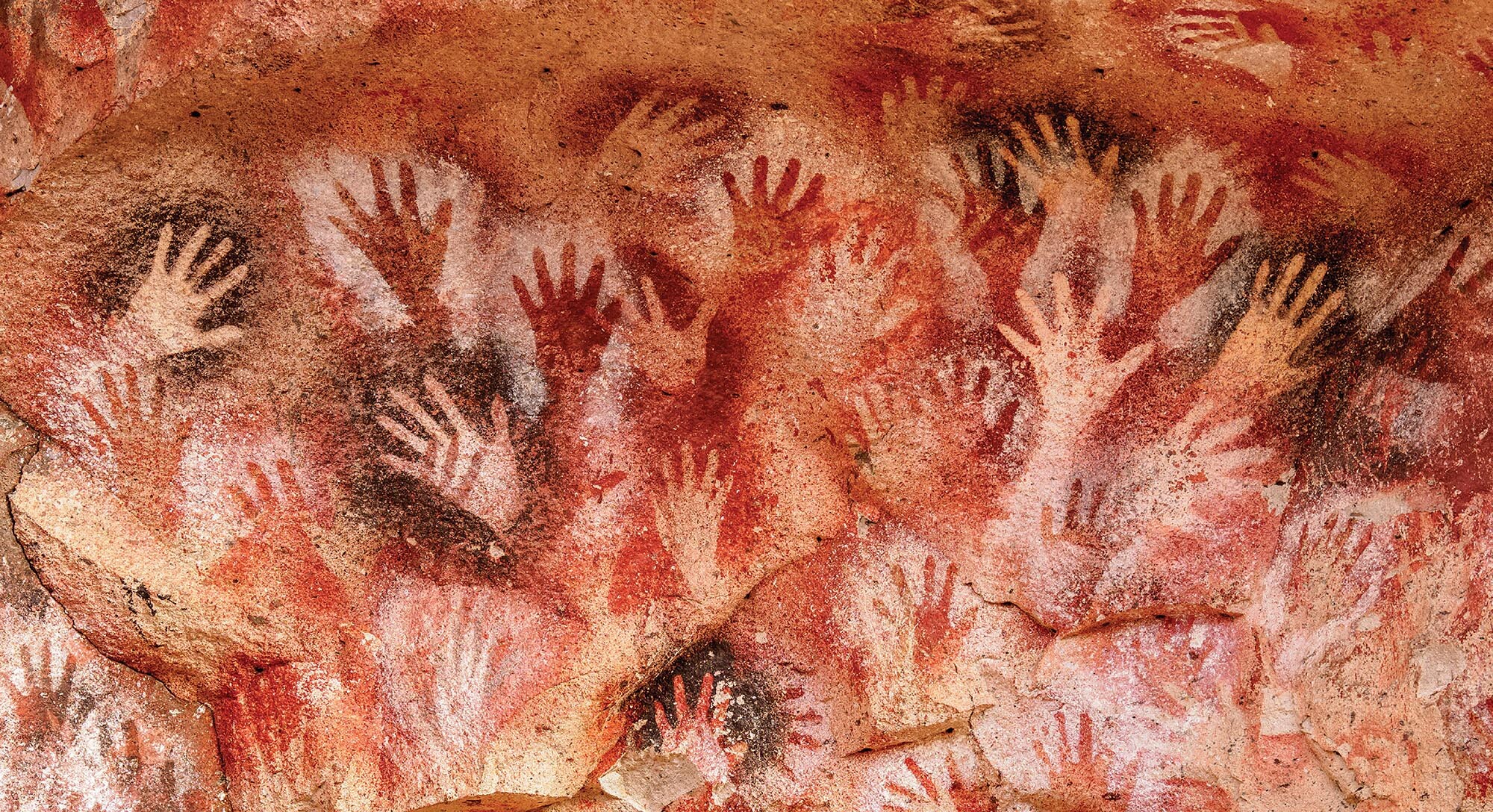 A painting on a rock wall features numerous handprints.