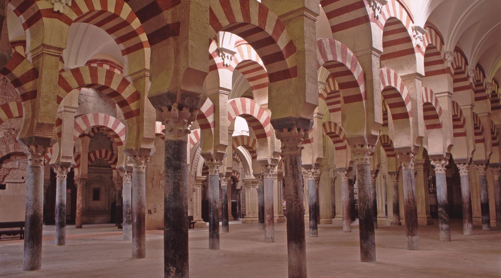 A side shot of a large open area in the Mosque of Cordoba that shows many columns in rows holding up arched ceilings.