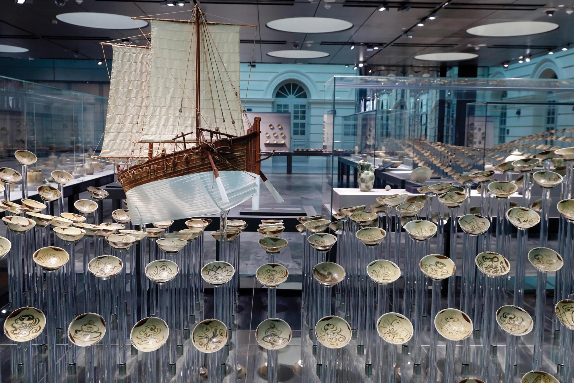 A photo of an exhibition of a wave of ceramics bowls on risers with a model ship in the center.