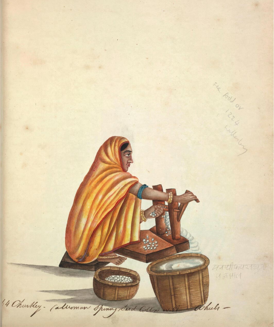 A woman sits sideways and removes seeds from cotton using an old traditional cotton ginning tool.