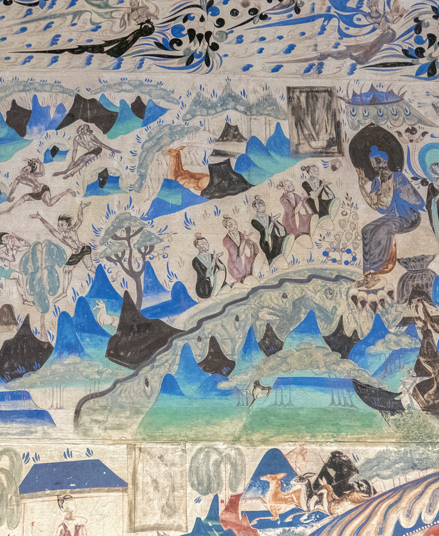 Mogao Cave mural showing Buddhist figures, floating spirits, and people gathered in a blue mountain landscape.