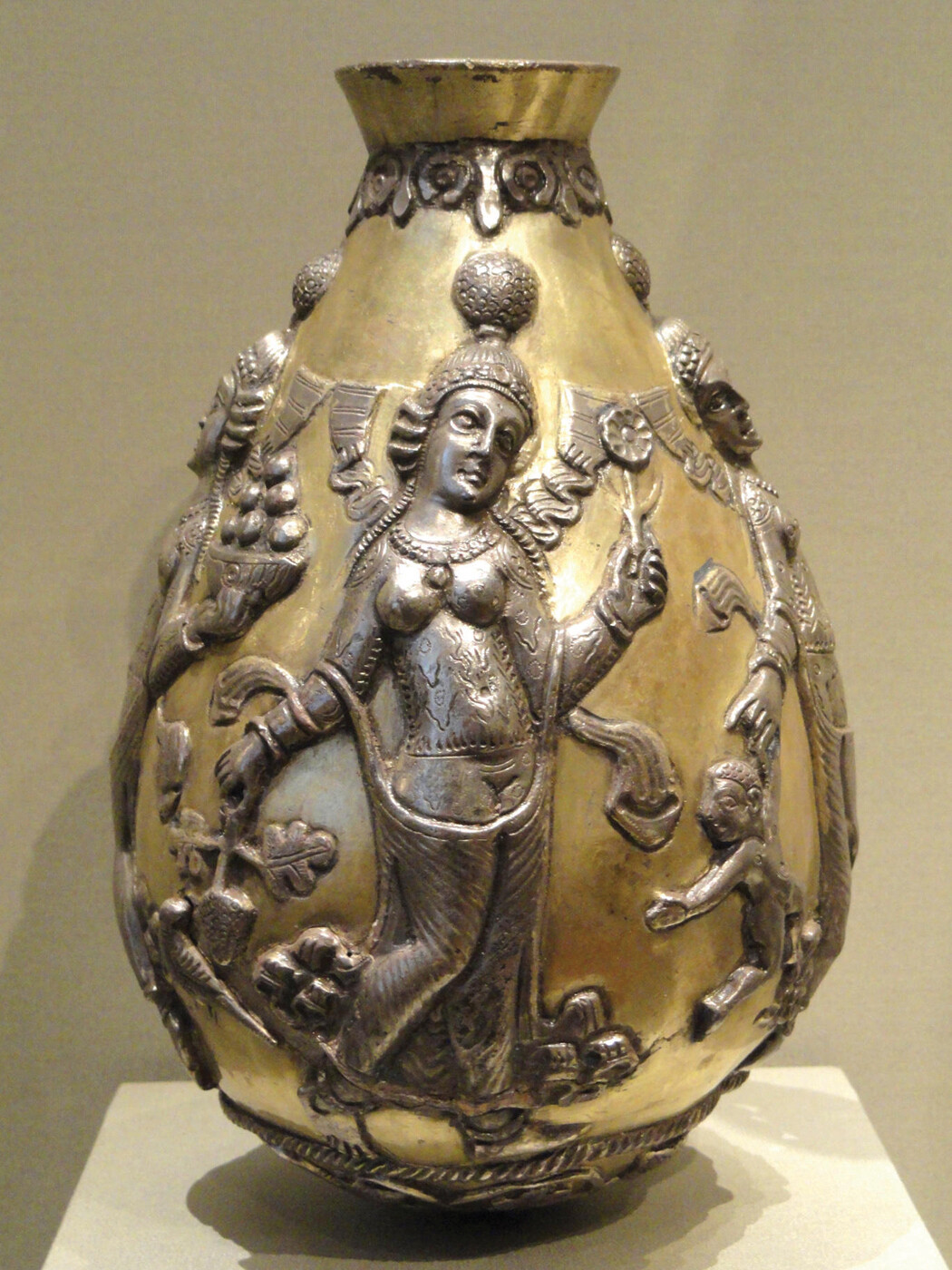 A Sasanian silver vessel with a rounded body and narrow neck is decorated with raised relief figures.