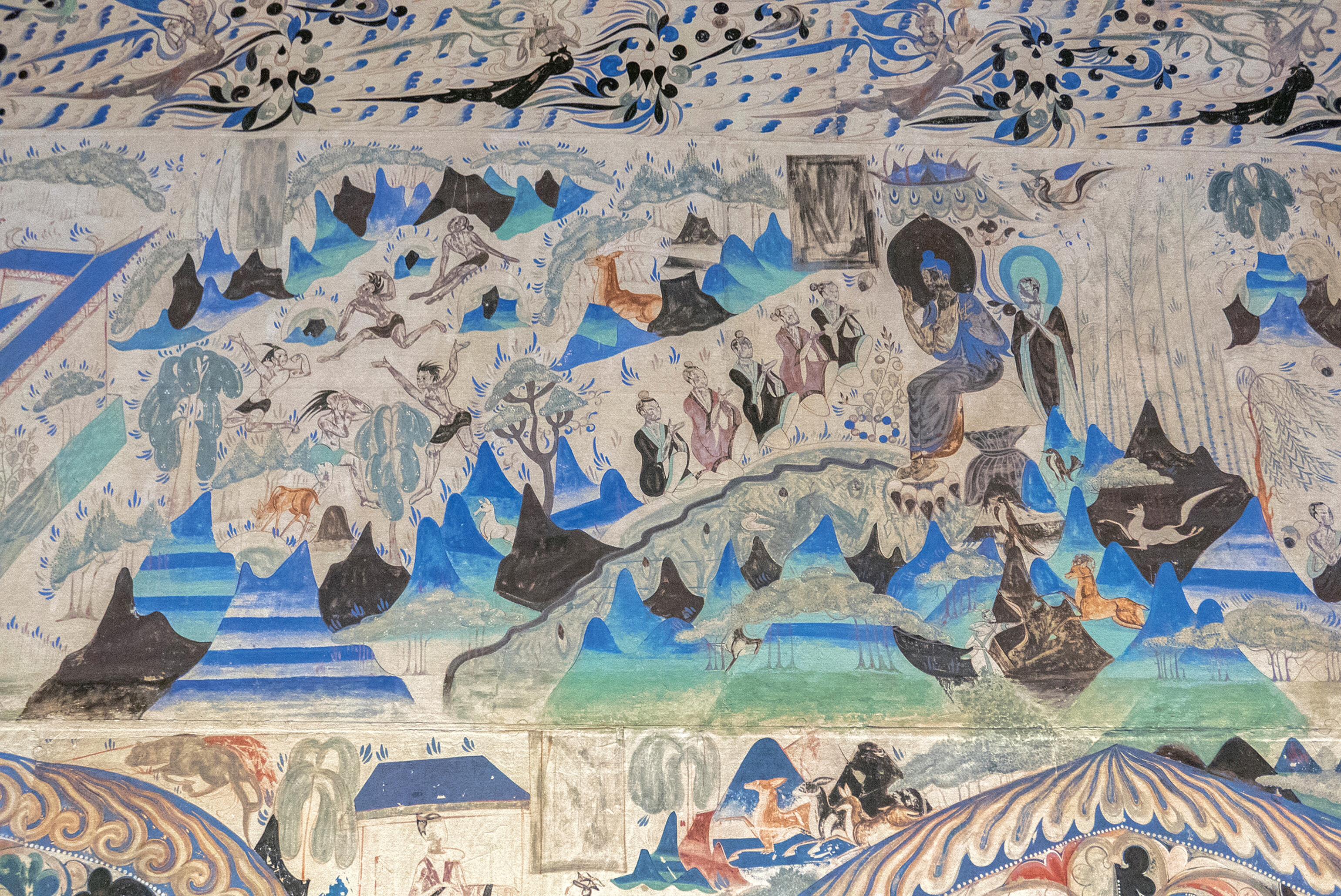Mogao Cave mural showing Buddhist figures, floating spirits, and people gathered in a blue mountain landscape.